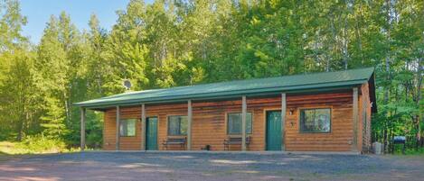 A rustic log cabin with a green roof, two benches outside, and a gravel driveway.