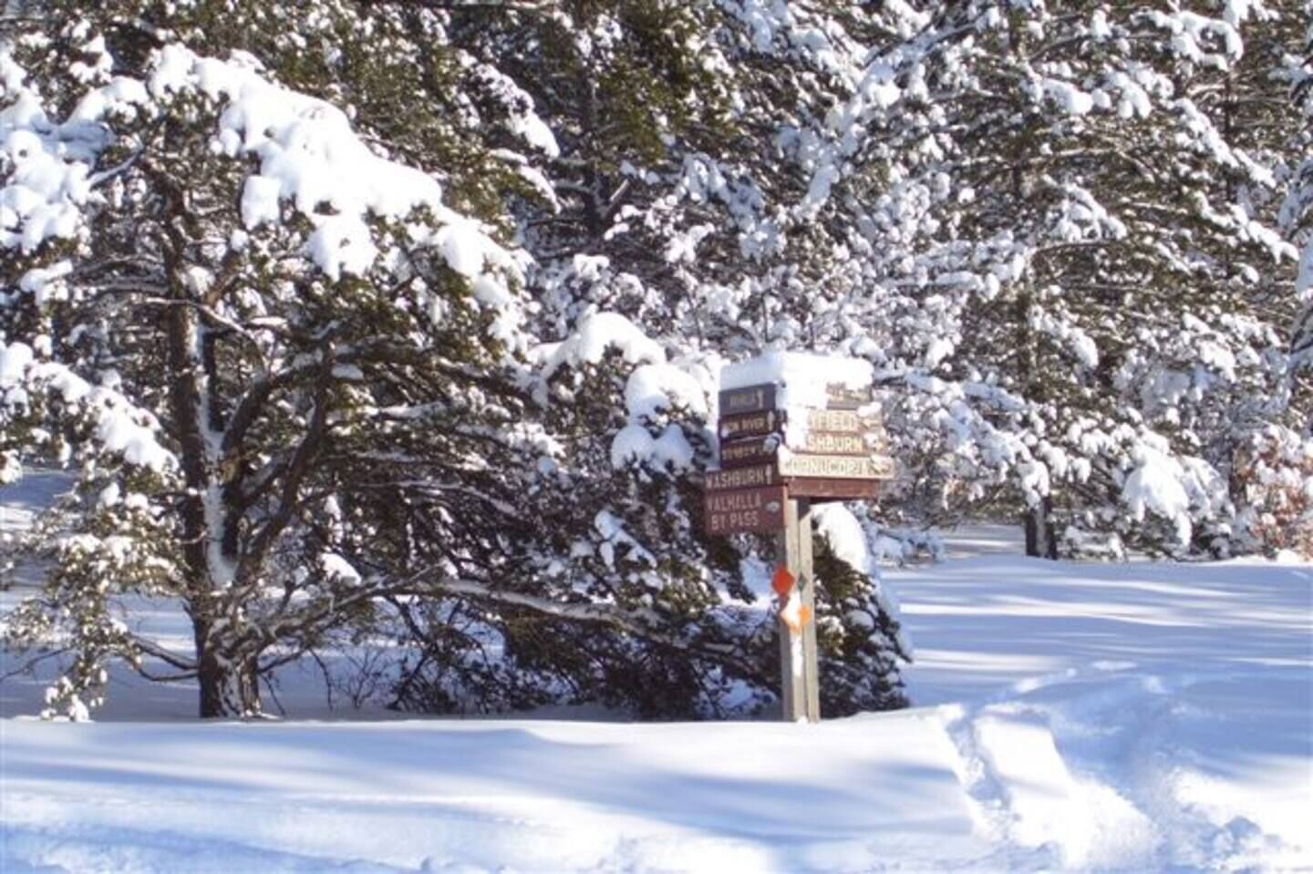 Paisaje nevado con un cartel que indica las direcciones a lugares cercanos.