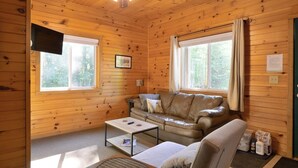 Un intérieur de chalet chaleureux avec un canapé en cuir, une table basse et un ventilateur de plafond.