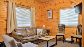 Une pièce confortable, aménagée comme un chalet, avec un canapé en cuir, une petite table, deux chaises et des murs en bois.