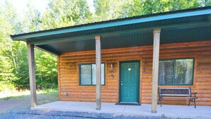 Une cabane en rondins avec une porte verte, un banc à l’extérieur et une allée gravillonnée.