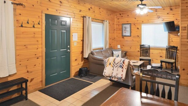 L’intérieur d’un chalet accueillant, avec une porte verte, un canapé, une table à manger et deux chaises.