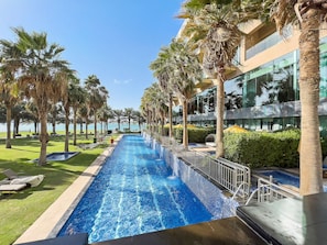 A swimming pool with a view of the sea, surrounded by palm trees and a modern building.