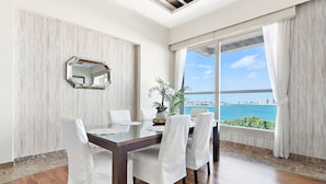 A modern dining room with a large table, white chairs, a decorative mirror, and a view of the ocean. - WelHome - Deluxe Apartment With Panoramic Sea Views (Dubai)