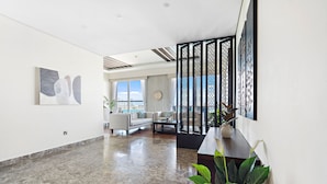 A spacious living area with a modern design, featuring a large window, a sofa, a coffee table, and a decorative screen. - WelHome - Deluxe Apartment With Panoramic Sea Views (Dubai)
