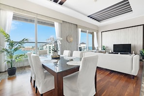A modern living room with a glass dining table, white chairs, a sofa, and a TV.