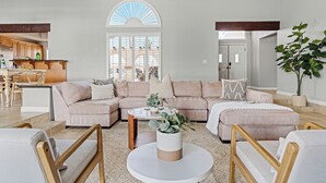 En moderne stue med en hjørnesofa, et sofabord og et stort vindue med udsigt udad.