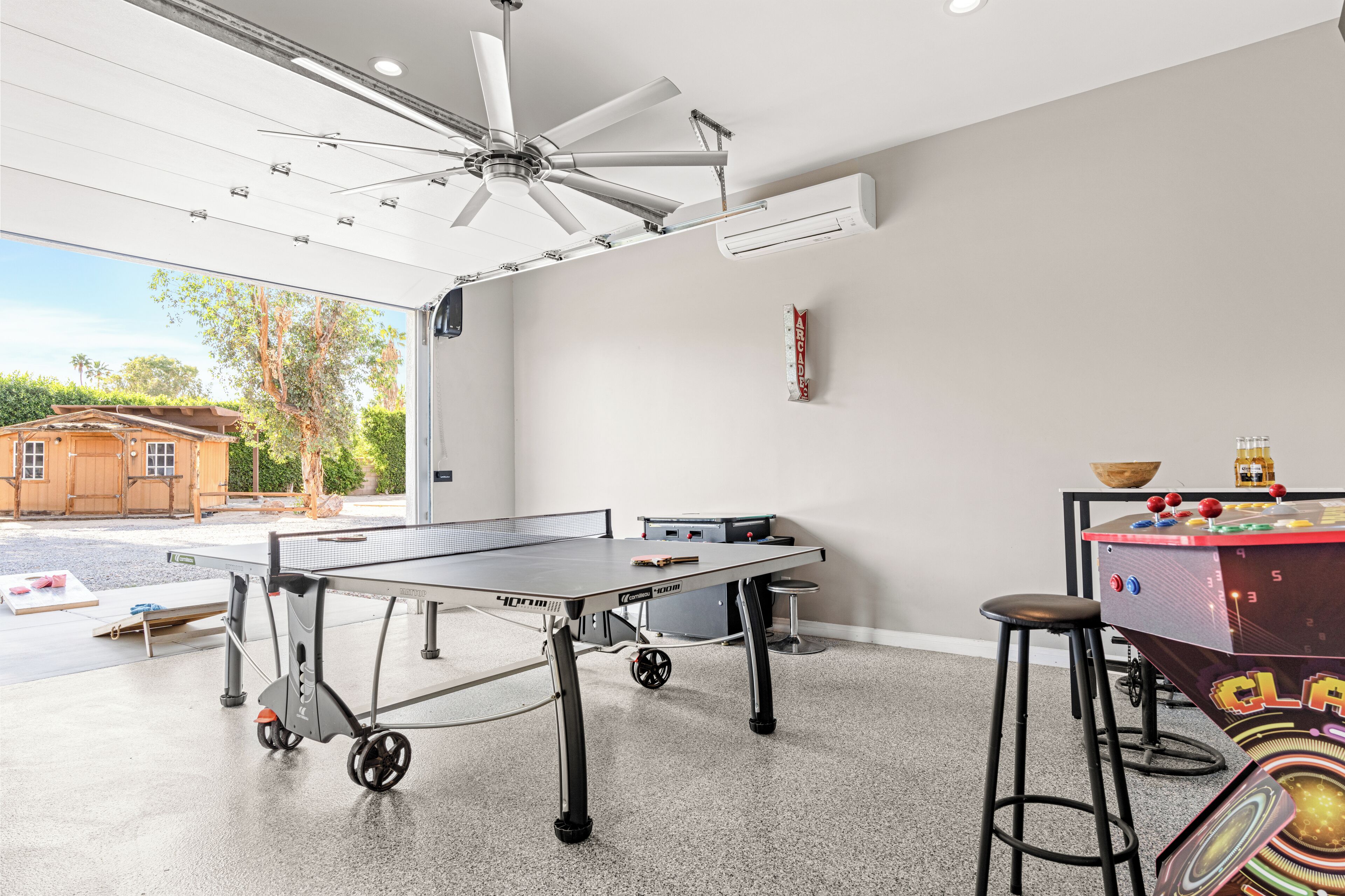 A ping pong table with a ceiling fan, a foosball table, and a bar area with stools.