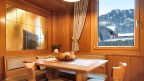 Een houten interieur met een eettafel, bankzitplaatsen, een fruitschaal en een raam met uitzicht op een besneeuwde berg.