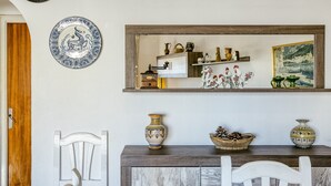 A dining area with a wooden cabinet, white chairs, a table, decorative plates, and a painting on the wall. - Apartment 'Sol Y Mar 2 Dorm Playa Riells' with Balcony (L'Escala)