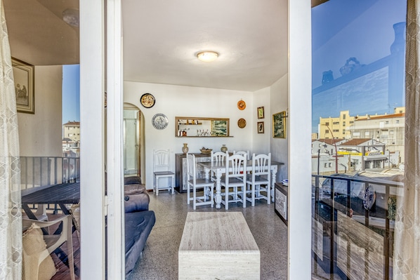 A living room with a sofa, a dining table with chairs, a coffee table, and a view of the city through a window.