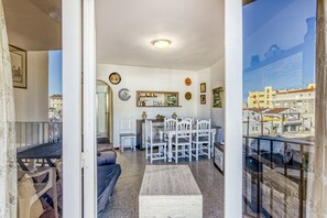 Una sala de estar con sofá, una mesa de comedor con sillas, una mesa de centro y vista a la ciudad por una ventana.