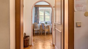 Un couloir mène à une salle à manger dotée d’un plancher en bois, d’une table avec des chaises et d’une fenêtre avec des rideaux.