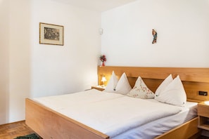 Una cama bien hecha con cabecera de madera, una mesita de noche con lámpara, un cuadro en la pared y una pequeña estatua.