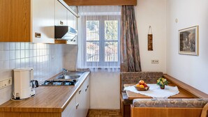 Une cuisine compacte équipée d’une cuisinière, d’un évier et d’une machine à café. On y trouve également un coin repas avec un banc et une table dressée avec des fruits et des fleurs.