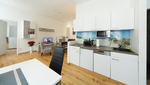 A modern kitchen with white cabinets, a microwave, and a coffee maker. There is a dining area with a table and chairs. - Apartment No. 13 in Vienna near Schönbrunn/Westbahnhof | Keyless Check-In (Wien)