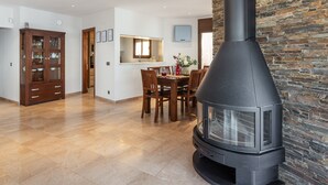 Ein modernes Wohnzimmer mit Kamin aus Stein, einem Holzespeisetisch und einer Küchenzeile mit großem Fenster.
