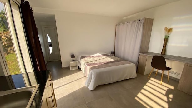 Een slaapkamer met een bed, nachtkastjes, een bureau en een stoel. Er is een raam met gordijnen, een wastafel en een vaas met bloemen op het bureau.