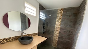 Een moderne badkamer met een stenen wastafel, een grote spiegel en een douchecabine met glazen wanden.