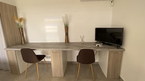 Een moderne keuken met een grijze aanrecht, twee bruine stoelen, een televisie en een airconditioner aan de muur.