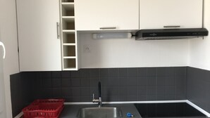 A modern kitchen with white cabinets, a black countertop, a red basket, and a built-in dishwasher. - Studio 3B108 - Résidence le Grand Large - Le Barcares (Le Barcarès)