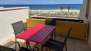 A balcony with a red table and chairs, overlooking a beach with a clear view of the sea and a few palm trees. - Studio 3B108 - Résidence le Grand Large - Le Barcares (Le Barcarès)