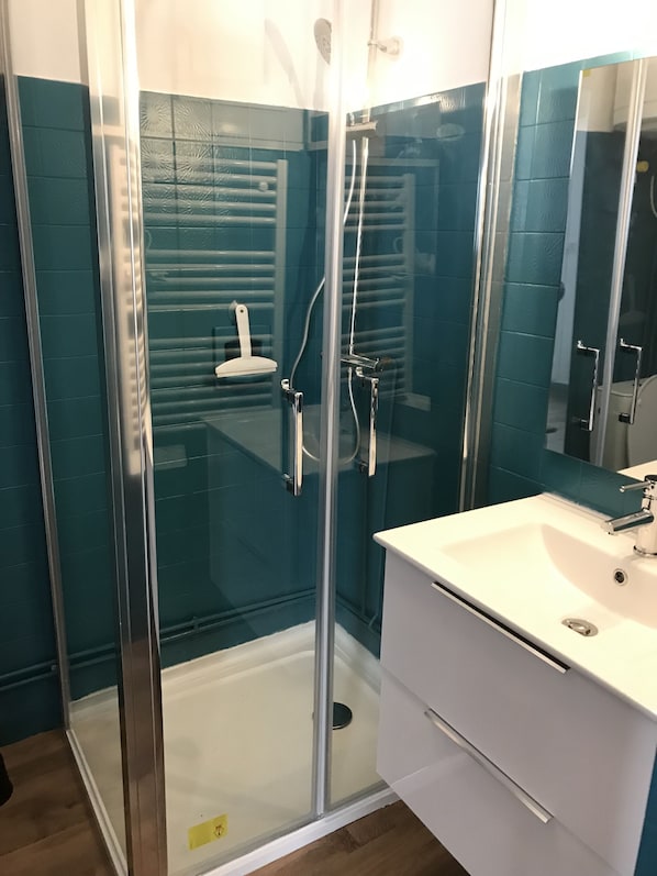 Een moderne badkamer met een douchecabine van glas, een wit wastafelmeubel en teal gekleurde wandtegels.