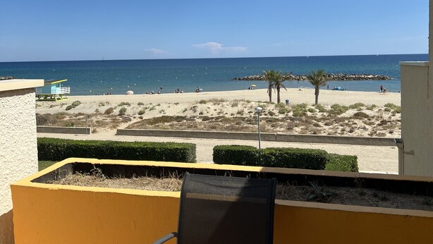 A balcony with a view of a beach, a lifeguard tower, and a palm tree. - Studio 3B108 - Résidence le Grand Large - Le Barcares (Le Barcarès)