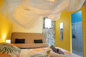 A bedroom with a bed, a sofa, a shower area, and a window with curtains. - 900m from the beach, the Bagatelle gites ** 2/4 pers, swimming pool and SPA (Sainte-Rose)