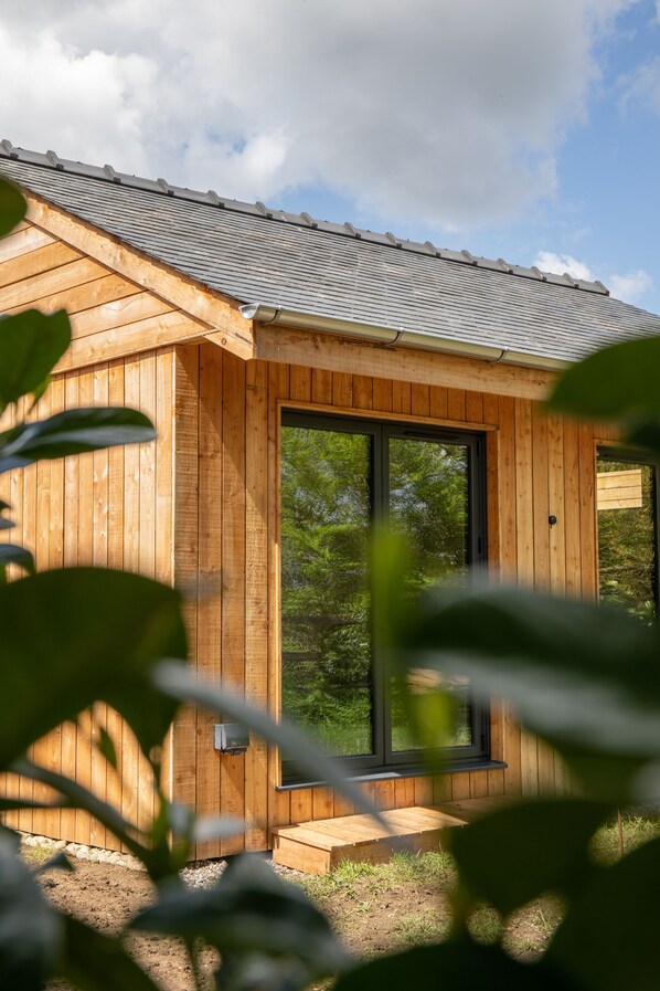 A wooden cabin with a sloped roof, large windows, and a wooden door. - The Weeping Willow Lodges (Bury St Edmunds)