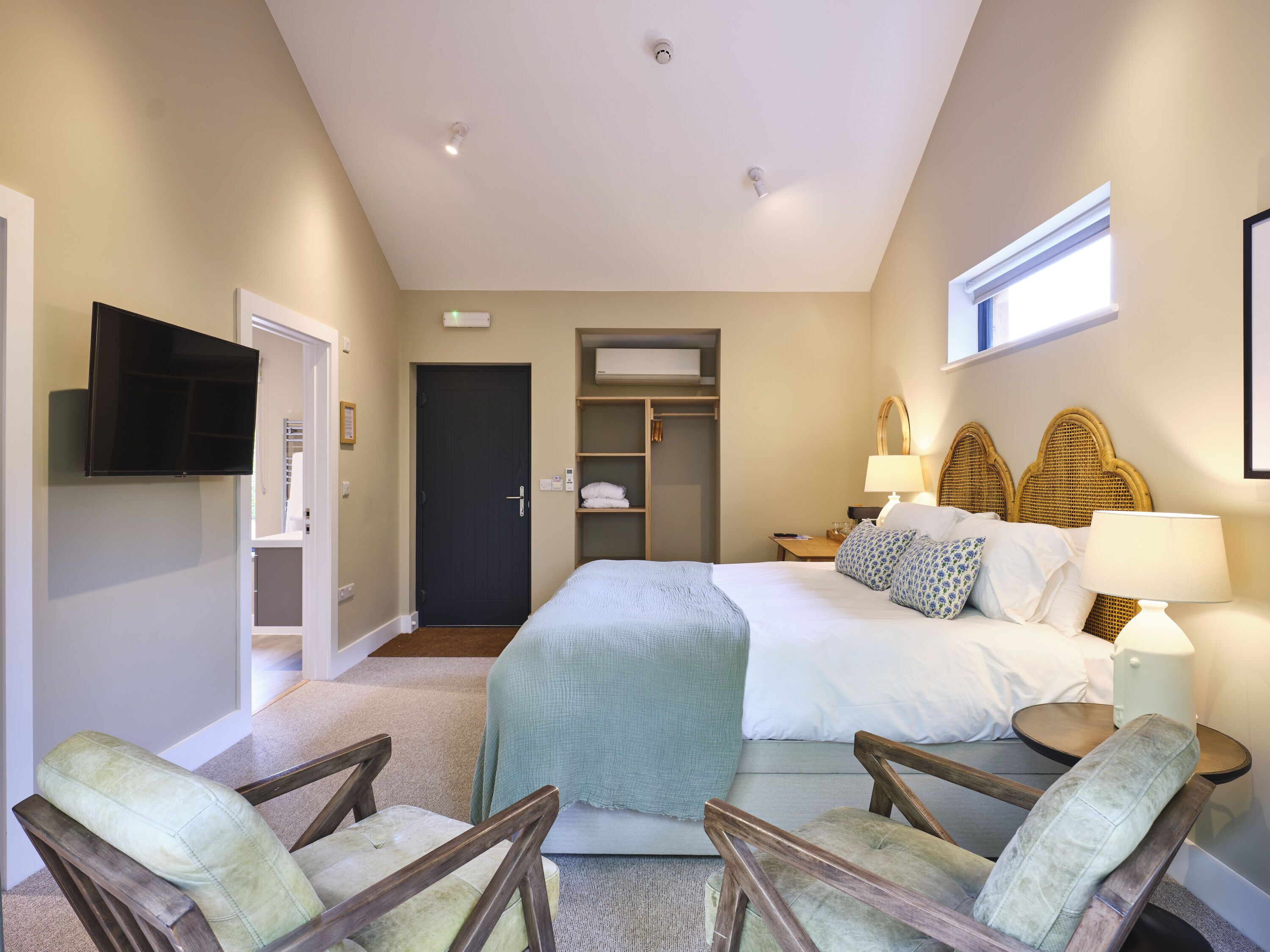A hotel room with a bed, two armchairs, a TV, a wardrobe, and a window.