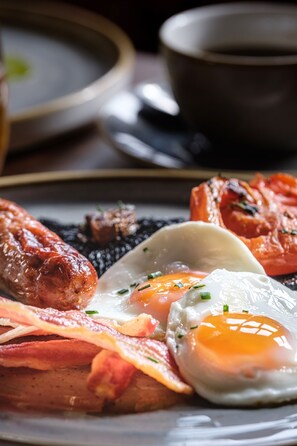 A breakfast plate with sausages, bacon, eggs, and a roasted tomato. - The Weeping Willow Lodges (Bury St Edmunds)