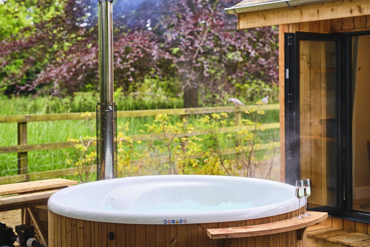 Een hottub met een houten terras, omgeven door een houten hek en weelderige begroeiing.