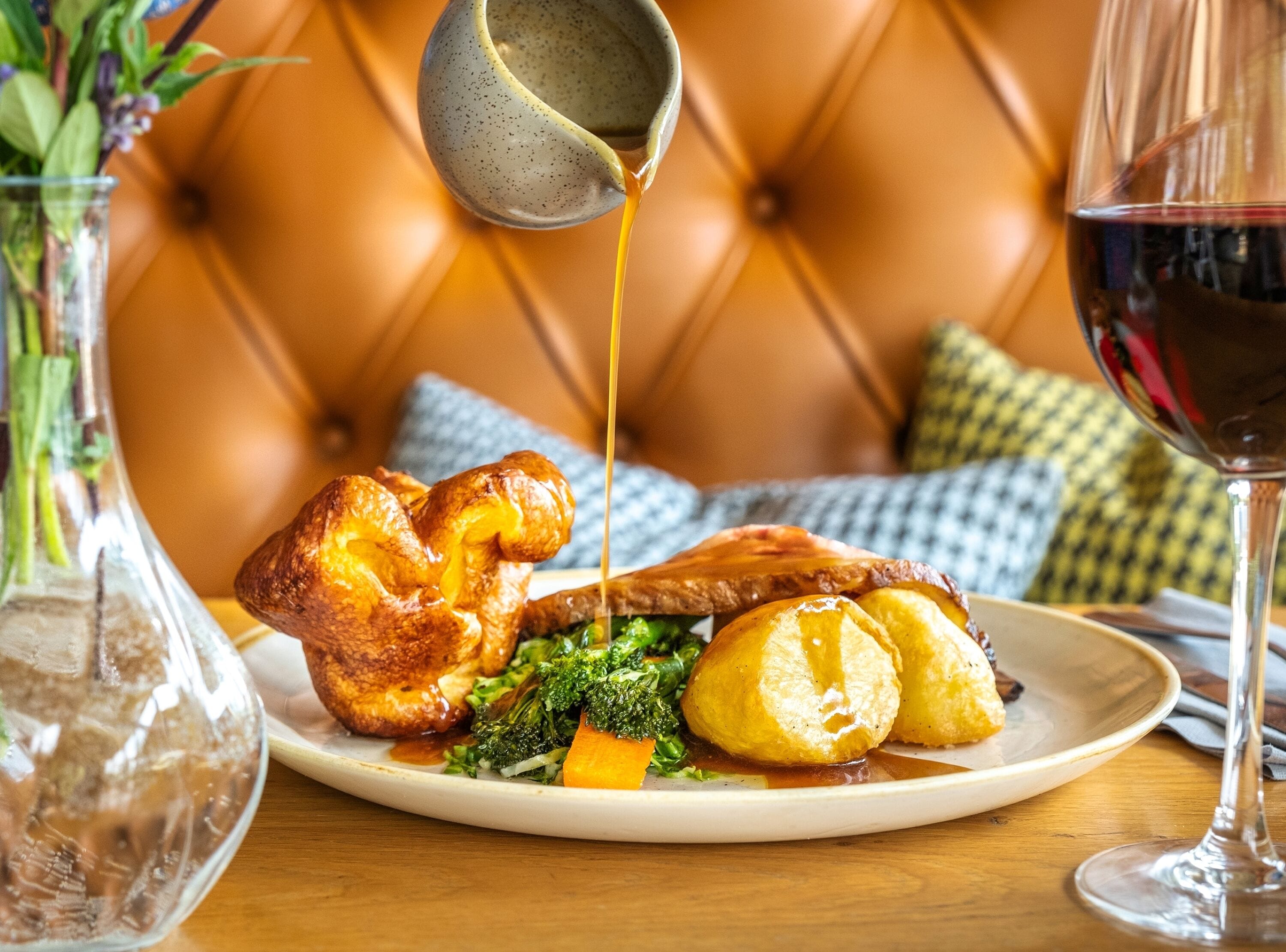 A plate with Yorkshire pudding, roast beef, and vegetables, a glass of red wine, and a vase with flowers.
