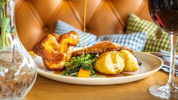 A plate with Yorkshire pudding, roast beef, and vegetables, a glass of red wine, and a vase with flowers.