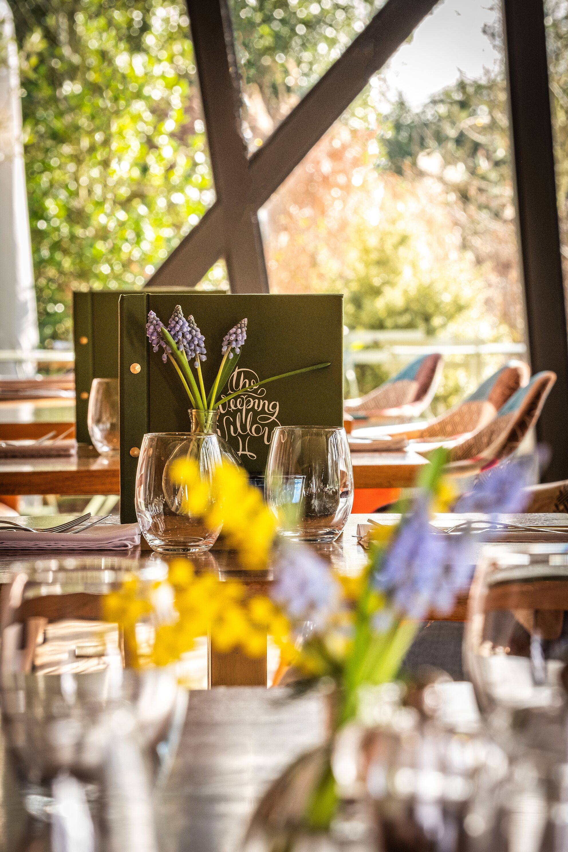 Een gedekte tafel met een menukaart, een vaas met bloemen en een glas.