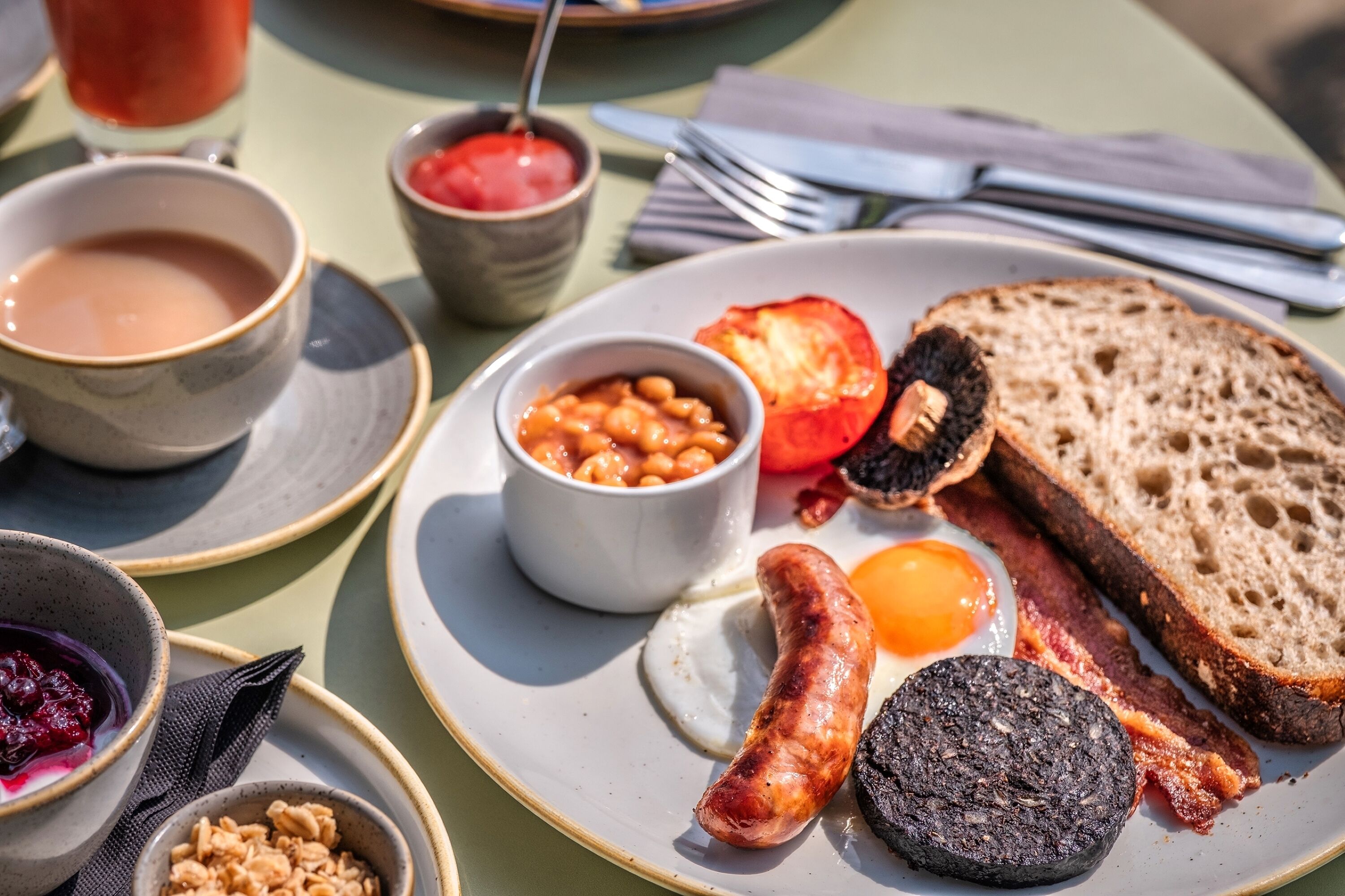 En frukosttallrik med ägg, bacon, korv, rostat bröd, bönor och en tomat.