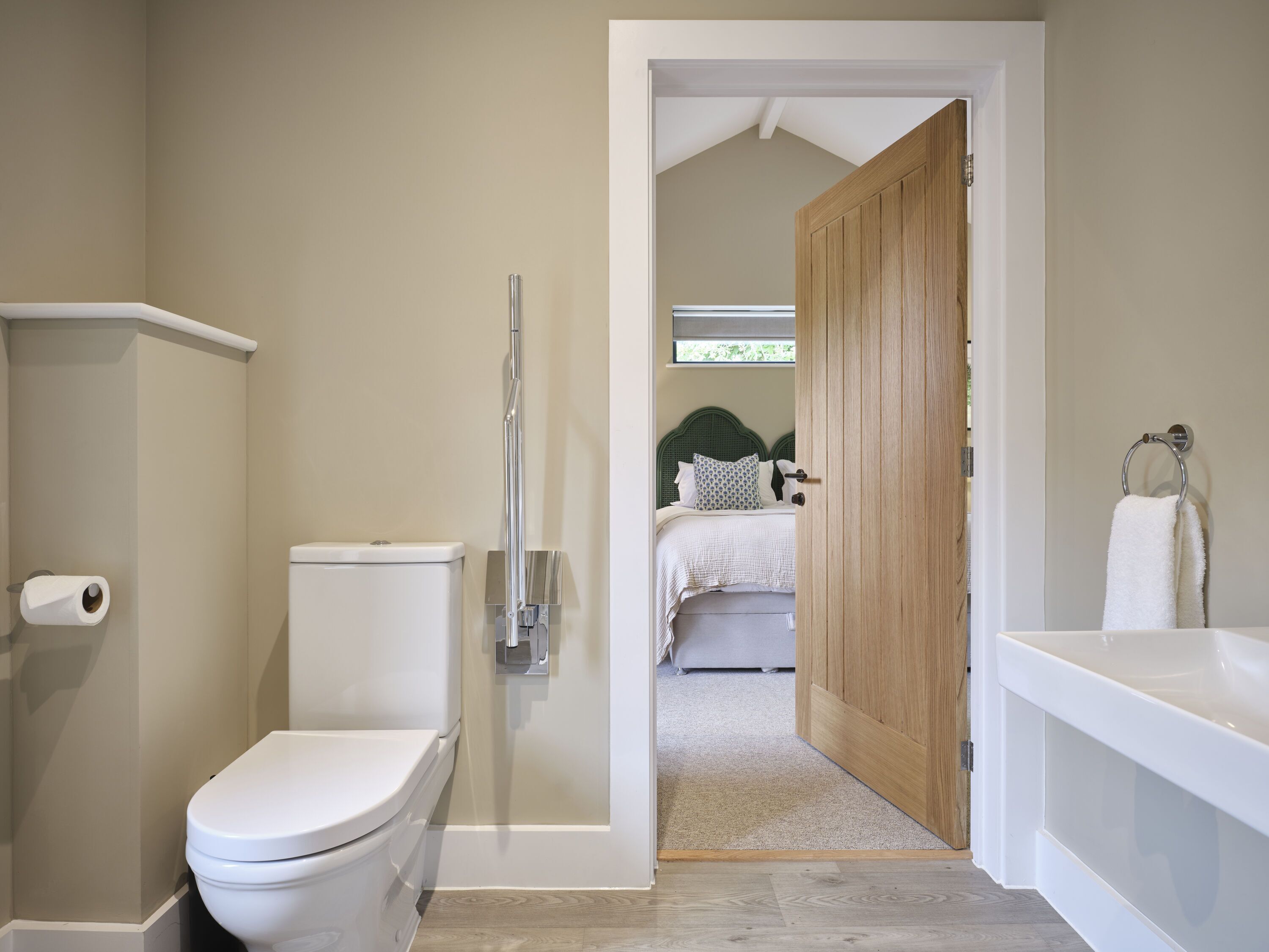 Une salle de bain équipée de toilettes, d’une douche et donnant sur une chambre à coucher par une porte ouverte.