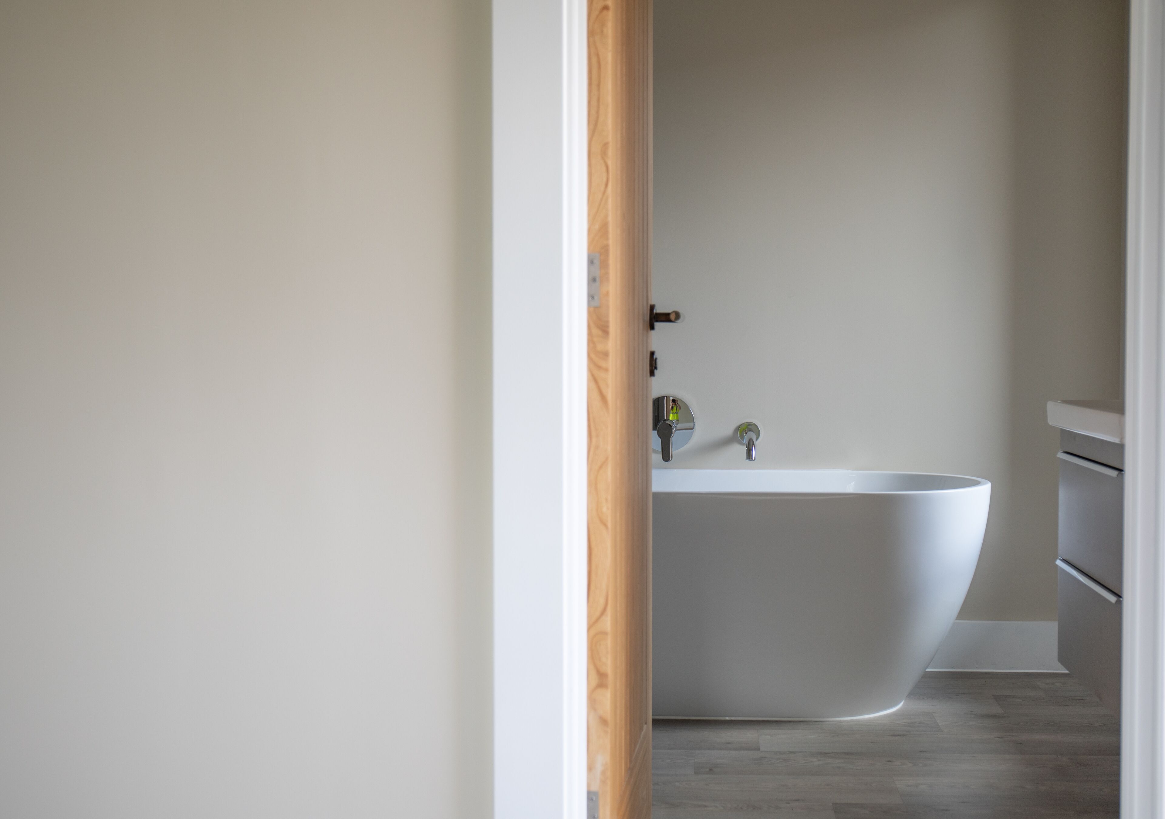 A modern bathroom with a freestanding bathtub, a minimalist sink, and a wooden door frame.