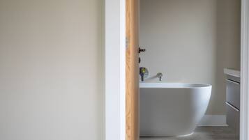A modern bathroom with a freestanding bathtub, a minimalist sink, and a wooden door frame.