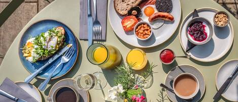 Una mesa de desayuno con distintos platos, como tostadas, huevos, frijoles y un croissant. También hay tazas de café y jugo.