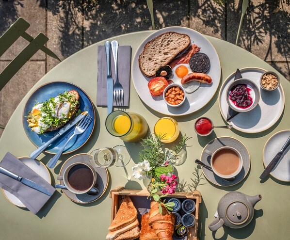 Una mesa de desayuno con distintos platos, como tostadas, huevos, frijoles y un croissant. También hay tazas de café y jugo.