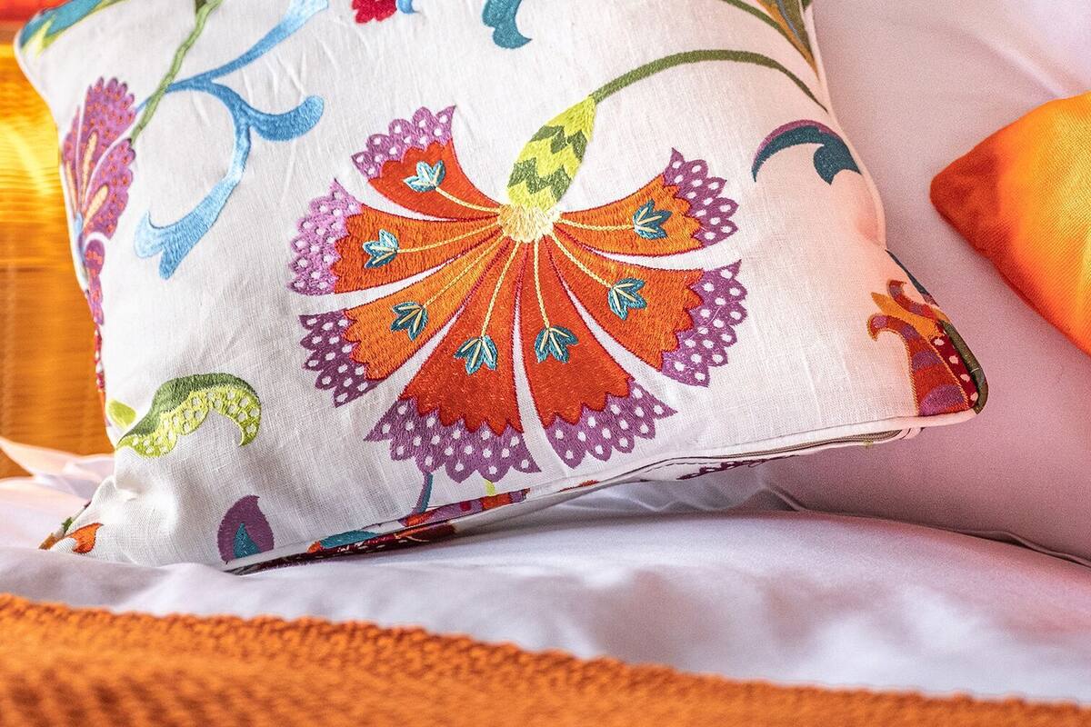 Een bed met een kleurrijk bloemenkussen en een gestreept lamp.