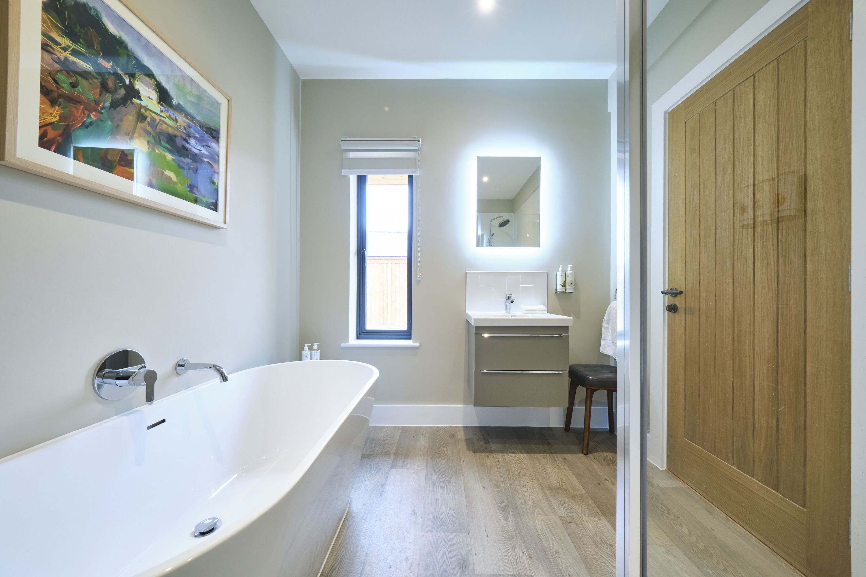 A modern bathroom with a freestanding bathtub, a vanity with a mirror, and a wooden door.
