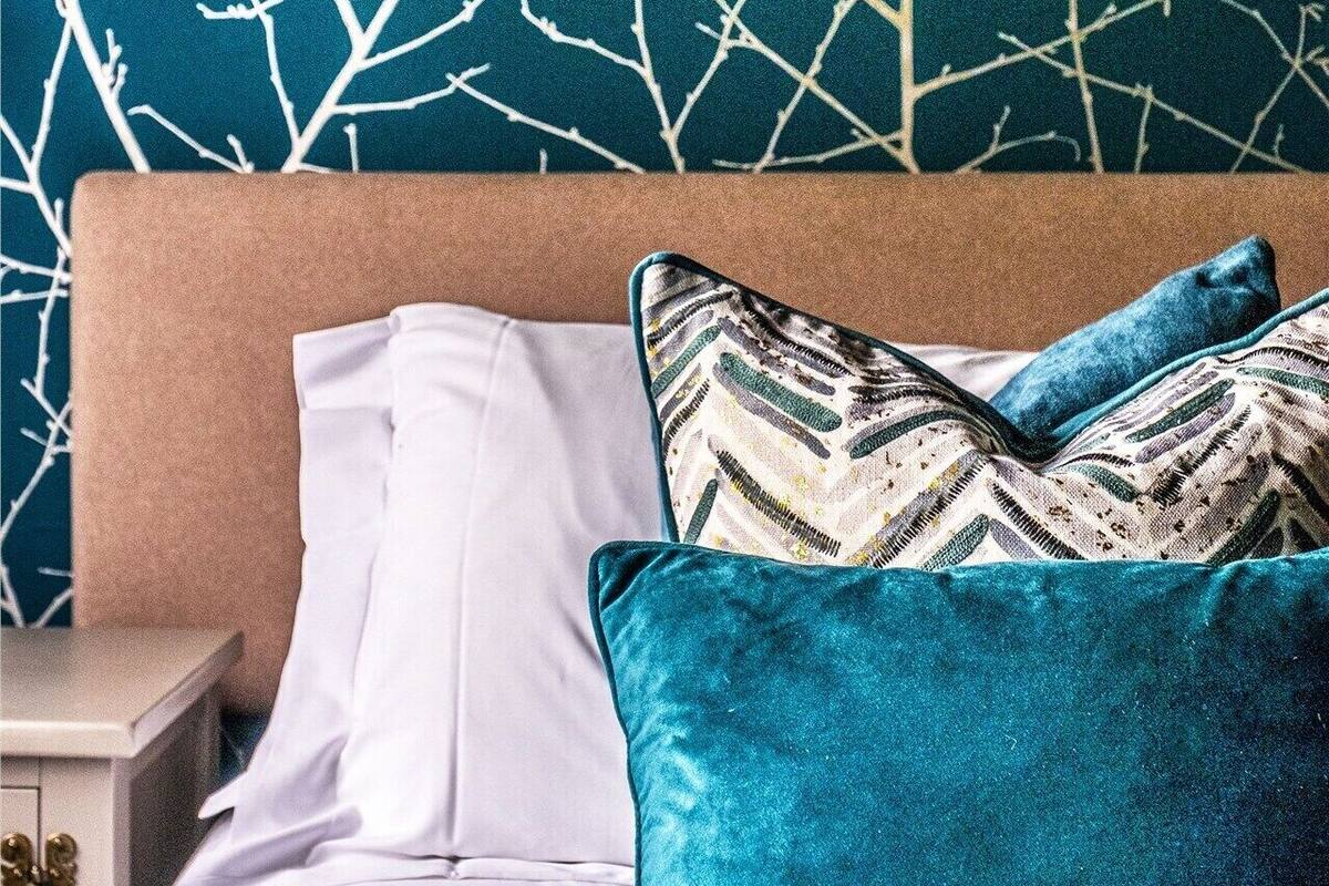 Een bed met een blauwgroen hoofdbord, witte kussens en een blauwe dekbedovertrek.