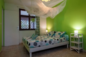 A bedroom with a bed, a bedside table, a lamp, a window with curtains, and a door. - Gites "villa bagatelle" ** 4/8 pers with swimming pool and SPA (Sainte-Rose)