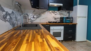 Una cocina con salpicadero de mármol, encimera de madera, armarios negros, un refrigerador blanco y un horno empotrado.