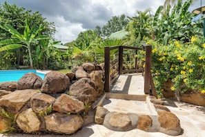 A stone pathway leading to a wooden pergola surrounded by tropical plants and a swimming pool. - Gites "villa bagatelle" ** 4/8 pers with swimming pool and SPA (Sainte-Rose)