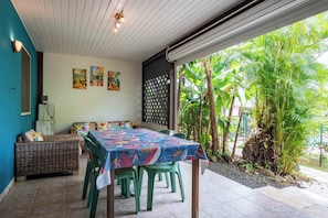 A dining area with a table covered in a colorful tablecloth, surrounded by chairs, and a sofa with cushions. - Gites "villa bagatelle" ** 4/8 pers with swimming pool and SPA (Sainte-Rose)