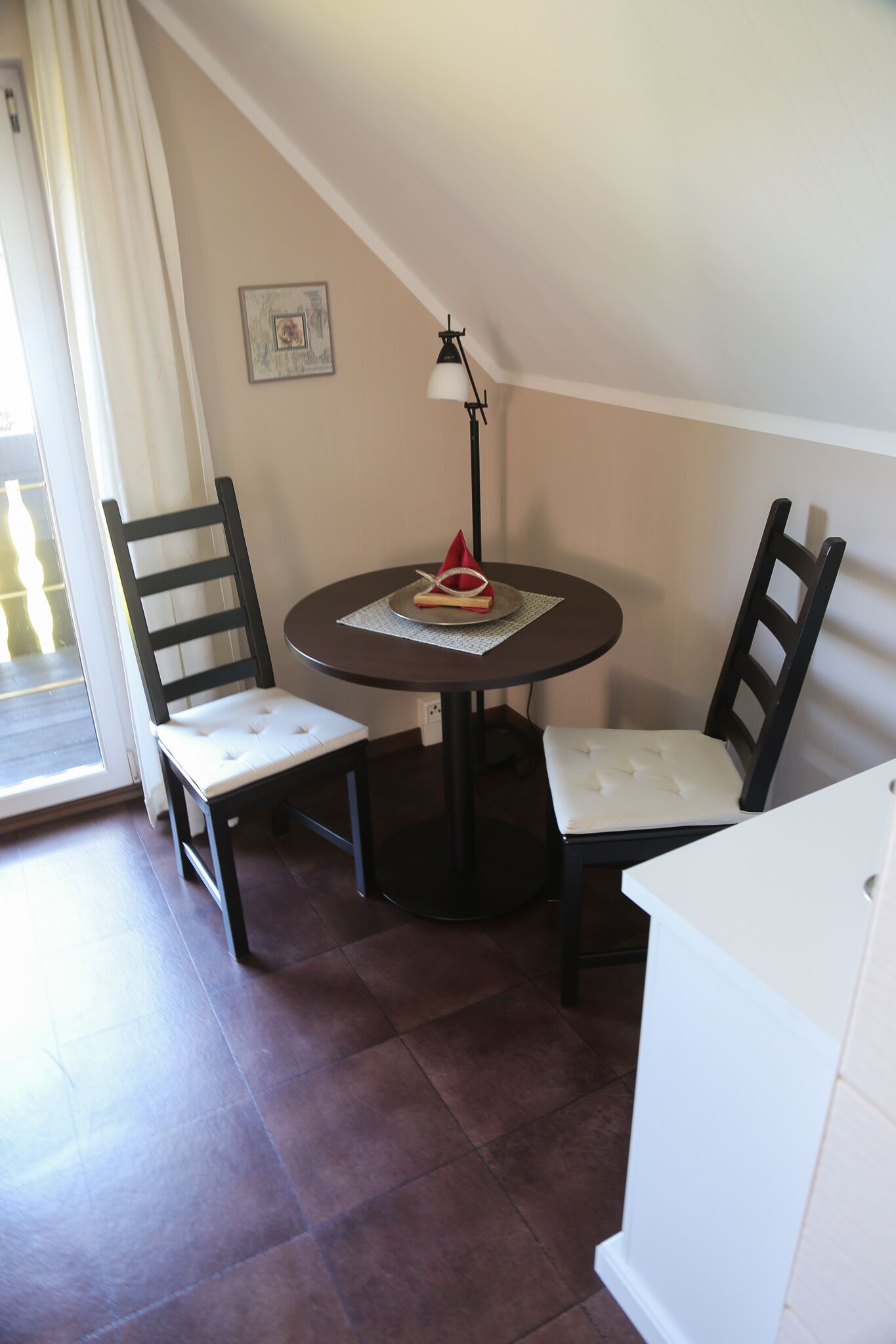 En spiseplads med et rundt bord, to stole, en lampe og en lille dekorativ genstand på bordet.